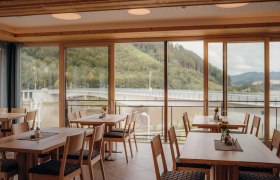 Die Donau und die Stadt Grein immer im Blick, © Niederösterreich Werbung/Daniela Führer Innenansicht eines Gasthofes mit großen Fenstern und Blick auf eine Brücke und bewaldete Hügel.