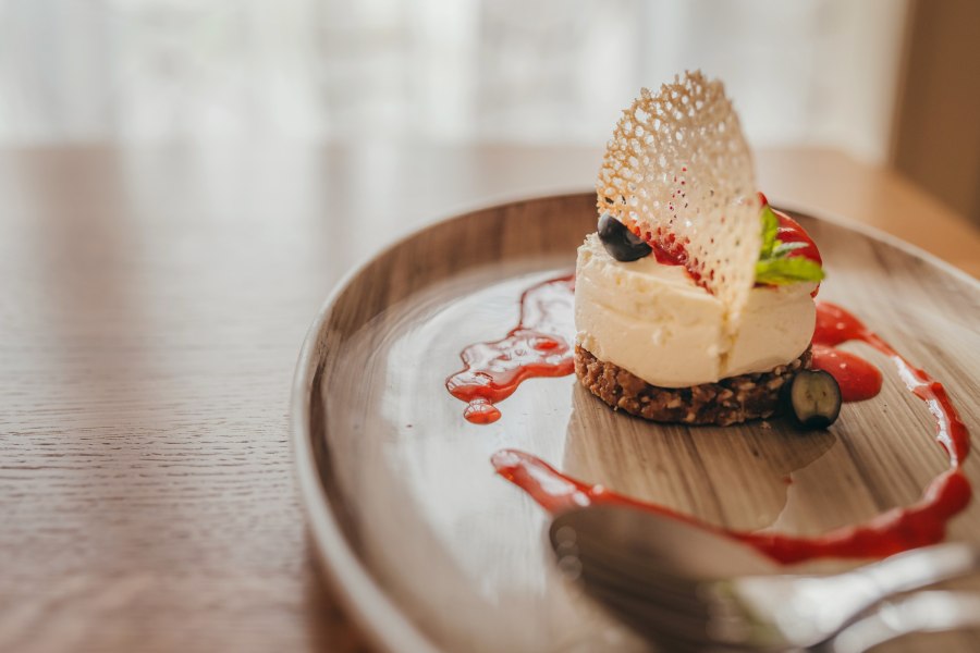 Mini-Käsekuchen mit Erdbeercoulis, © Niederösterreich Werbung/Daniela Führer Mini-Käsekuchen mit Erdbeercoulis auf einem Teller serviert.
