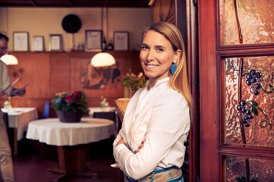 Wirtin Vera Baumgartlinger, © Niederösterreich Werbung/Andreas Hofer Frau in weißem Hemd lächelt in traditionellem Restaurant mit Holzeinrichtung.