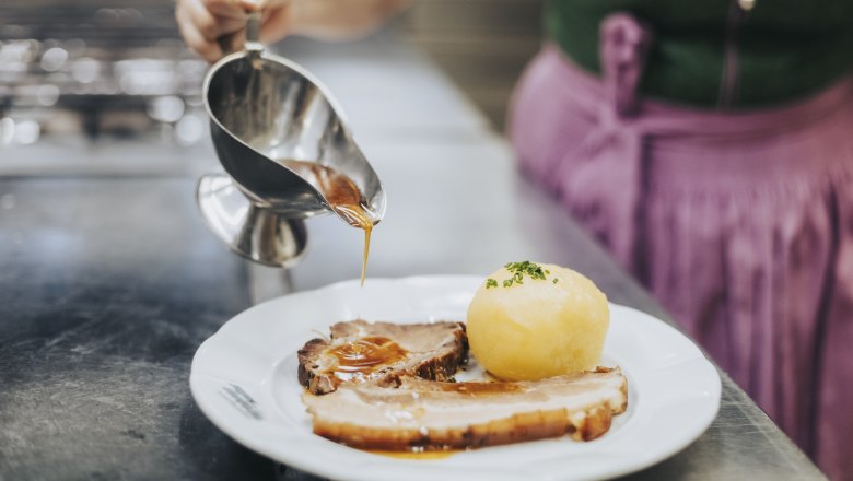 Hausmannskost von Karpfen bis Sonntagsbraten, © Niederösterreich Werbung/David Schreiber Eine Person gießt Soße über einen Teller mit Braten und Knödel.
