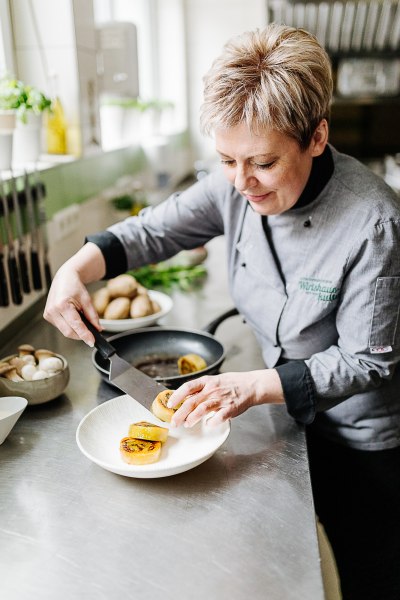 Wirtin Monika Hag, © Niederösterreich Werbung/Mara Hohla Eine Frau in Kochkleidung richtet Essen auf einem Teller an.