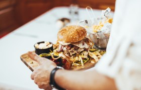 Regionaler Burger nach 7 Hirtner Art, © Niederösterreich Werbung/David Schreiber Ein Burger mit Sesambrötchen, Speck und Spiegelei auf einem Holzbrett, serviert mit Pommes und Dips.
