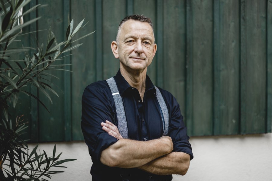 Für die Gäste da: Wirt Hans-Joachim Beringer, © Niederösterreich Werbung/David Schreiber Ein Mann in dunklem Hemd und Hosenträgern steht mit verschränkten Armen vor einer grünen Holzwand.