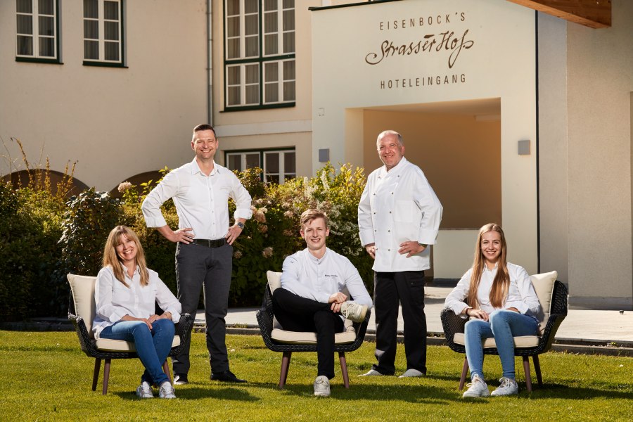 Familie Eisenbock & Chefkoch Christian Schimann, © Niederösterreich Werbung/Andreas Hofer Fünf Personen posieren vor einem Gebäude mit der Aufschrift 'Eisenbock's Strasserhof Hoteleingang'.