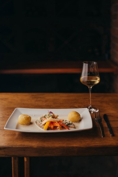 Krenfleisch vom Weiderind, Wurzelgemüse, Knödel, © Niederösterreich Werbung/Daniela Führer Ein Teller mit Krenfleisch, Wurzelgemüse und Knödeln auf einem Holztisch, daneben ein Glas Weißwein.