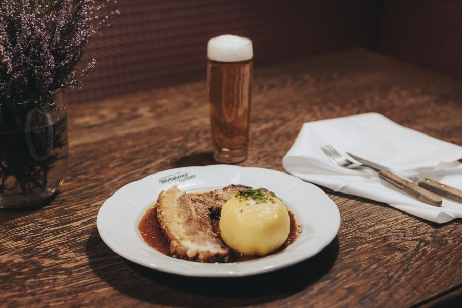 Schweinsbraten mit Waldviertler Knödel, © Niederösterreich Werbung/David Schreiber Ein Teller mit Schweinsbraten und Waldviertler Knödel, daneben ein Glas Bier auf einem Holztisch.