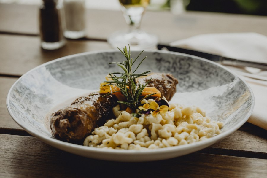 Rindsroulade, © Niederösterreich Werbung/Sophie Menegaldo Ein Teller mit Rindsroulade, Spätzle und Gemüse, garniert mit Rosmarin und essbaren Blüten.