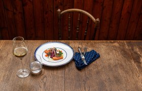 Bratapfel, geschmorter Radiccio, Lachsforelle, © Rita Newman Weißer Teller mit Bratapfel und Lachsforelle auf Holztisch.