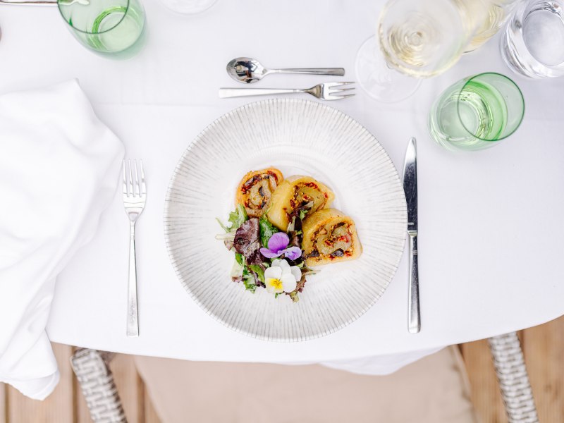 Gefüllte Erdäpfelroulade, © Niederösterreich Werbung/Mara Hohla Ein Teller mit gefüllter Erdäpfelroulade und Salat auf einem gedeckten Tisch.