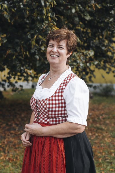 Wirtin: Anita Scheiterer, © Niederösterreich Werbung/David Schreiber Frau in traditioneller Tracht vor einem Baum im Freien.