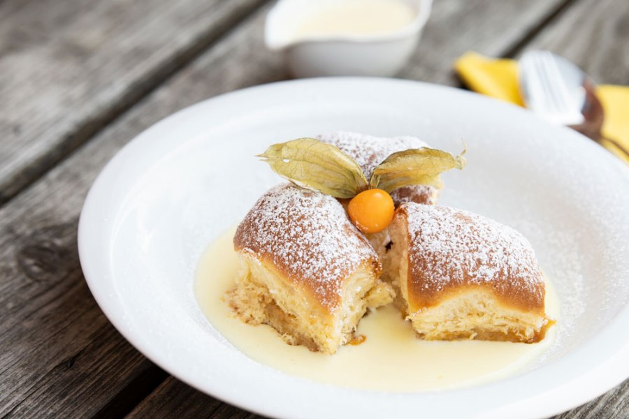 Freitags: Buchteln mit Vanillesauce, © Niederösterreich Werbung/Nadja Büchler Drei Buchteln mit Puderzucker und Physalis auf Vanillesauce auf einem weißen Teller.