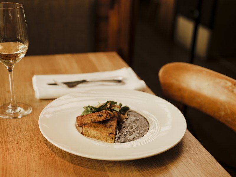 Erdäpfelterrine mit Herbsttrompetensauce, © Niederösterreich Werbung/Michael Reidinger Elegantes Gericht mit Wein auf Holztisch in stilvollem Restaurant.