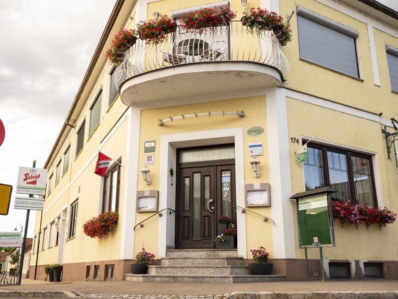 Wirtshaus mit 4-Sterne –Gästezimmern, © Niederösterreich Werbung/Michael Reidinger Gelbes Wirtshaus mit Blumen und Schildern, darunter "Stiegl" und "Retzerlandhof".
