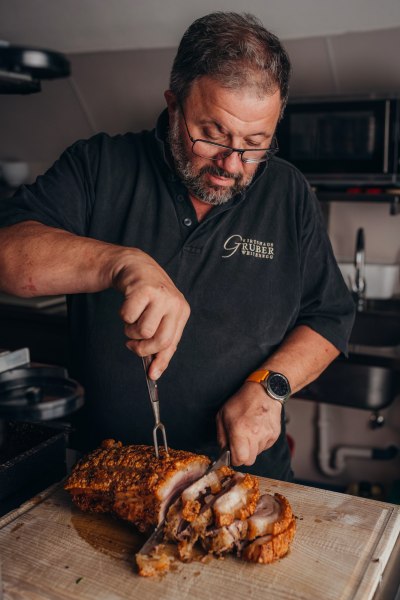 Küchenchef Johann Gruber, © Niederösterreich Werbung/Daniela Führer Mann schneidet knusprigen Schweinebraten in einer Küche.