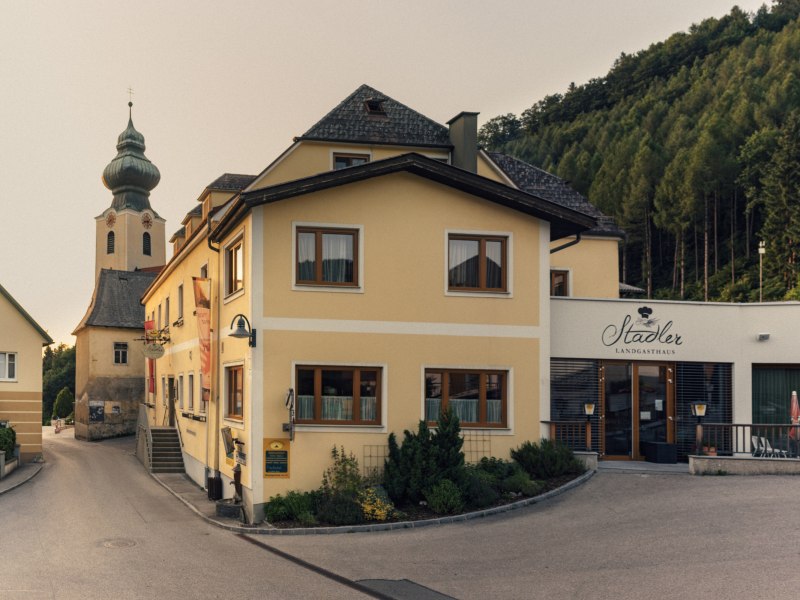 Wirtshaus in Reinsberg, © Niederösterreich Werbung/Julius Hirtzberger Gelbes Gebäude mit der Aufschrift 'Stadler Landgasthaus' und einer Kirche im Hintergrund.
