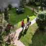 Anreise im Gasthof "Zum goldenen Anker", © Martina Siebenhandl Zwei Personen gehen auf einem gepflasterten Weg durch einen grünen Garten mit Tisch und Stühlen.