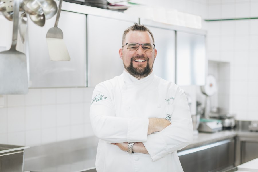 Christian Heissenberger, © Niederösterreich Werbung/David Schreiber Ein lächelnder Koch in weißer Uniform steht in einer professionellen Küche.