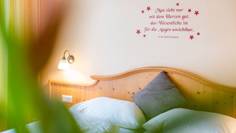 Zimmer zum Wohlfühlen, © Kremsl Gemütliches Schlafzimmer mit Zitat an der Wand und Holzkopfteil.