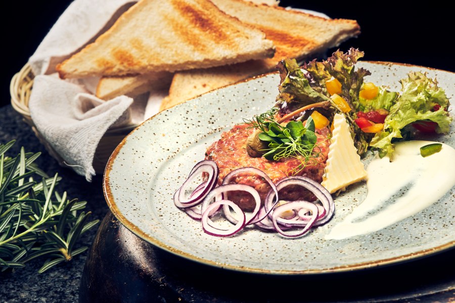 Beef Tatar, © Niederösterreich Werbung/Andreas Hofer Ein Teller mit Beef Tatar, Zwiebelringen, Salat und Toastscheiben.