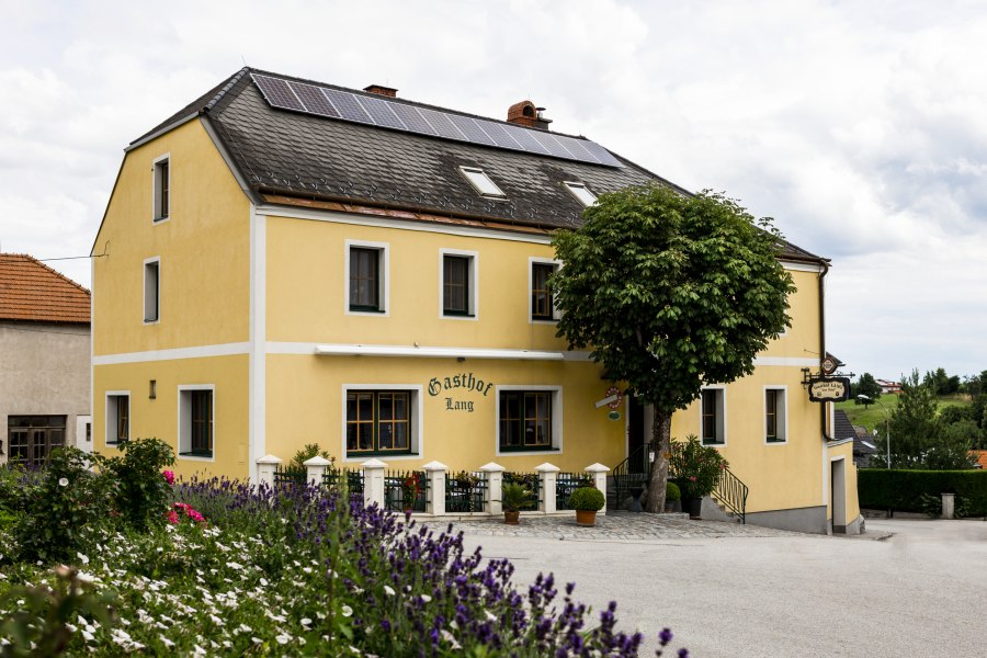 Wirtshaus in Weinzierl am Walde, © Niederösterreich Werbung/David Schreiber Gelbes Gasthaus mit Solarpanelen auf dem Dach, umgeben von Blumen und Bäumen.