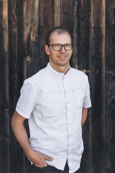 Andreas Mathe, © Niederösterreich Werbung/David Schreiber Mann mit Brille und weißem Hemd vor Holzwand.