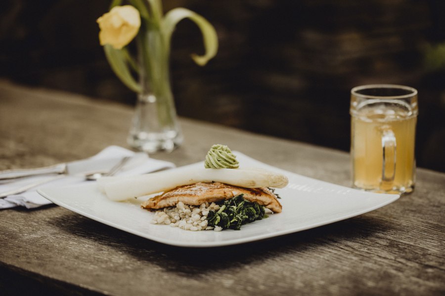 Zarter Fisch trifft knackigen Spargel, © Niederösterreich Werbung/Sophie Menegaldo Gourmetgericht mit Spargel, Fisch und Gemüse auf Holztisch, gelbe Blume im Hintergrund.