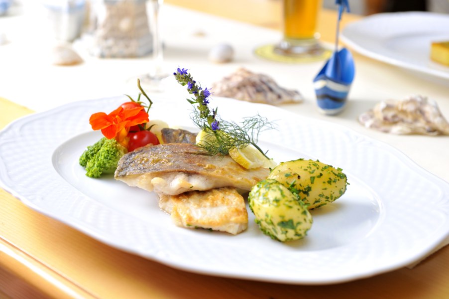 Ausgezeichnet mit Waldviertler Karpfen-Haube, © Waldviertel Tourismus/Robert Herbst Ein Teller mit gebratenem Fischfilet, Kartoffeln und Gemüse, dekoriert mit Kräutern und Blüten.