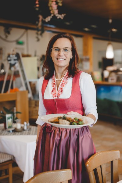 Wirtin Christiane Rabl, © Niederösterreich Werbung/ David Schreiber Frau in traditioneller Tracht serviert ein Gericht in einem Restaurant.