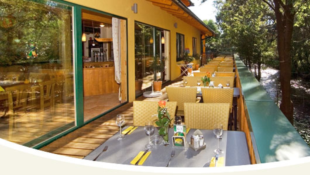 Naturfreunde Bootshaus, © Bootshaus Terrasse eines Restaurants mit gedeckten Tischen und Blick auf einen Fluss.