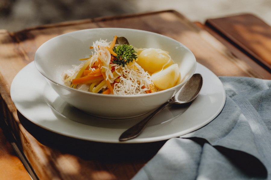 Krenfleisch vom Schweinsbauch, Wurzelstreifen, Salzerdäpfel, © Niederösterreich Werbung/Rita Newman Ein Teller mit Krenfleisch, Wurzelstreifen und Salzerdäpfeln, garniert mit Petersilie, auf einem Holztisch.