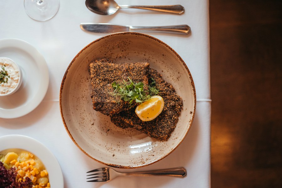 Waldviertler Karpfenfilet vom Stift Zwettl in Graumohn paniert, © Niederösterreich Werbung/Daniela Führer Graumohn-paniertes Karpfenfilet mit Zitronenscheibe und Kräutern auf Teller, daneben Beilagen.