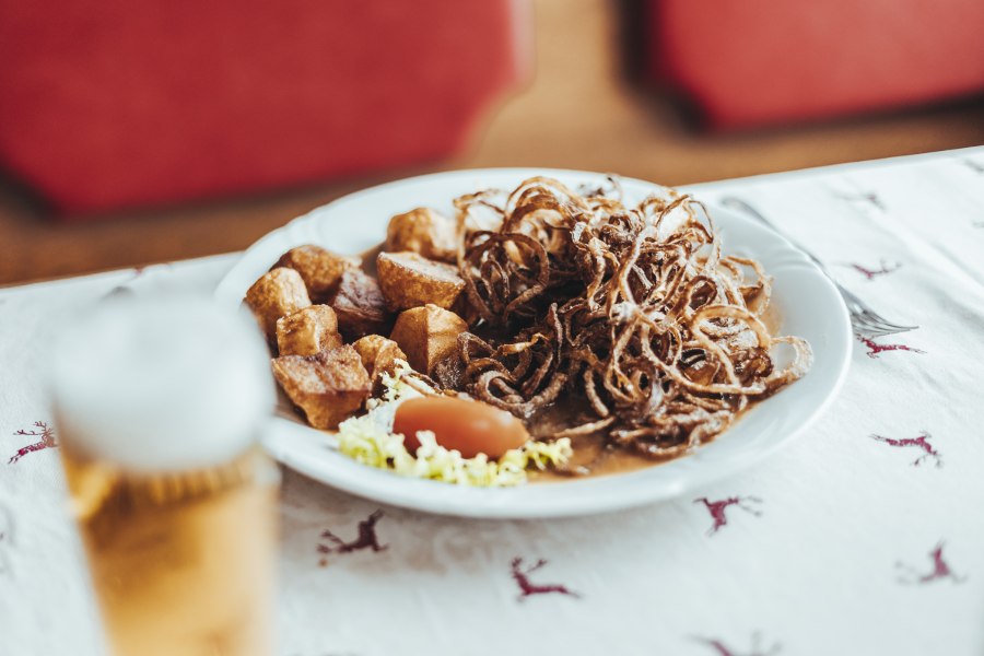 Zwiebelrostbraten mit Braterdäpfeln, © Niederösterreich Werbung/David Schreiber Ein Teller mit Zwiebelrostbraten, Braterdäpfeln und Salat auf einem Tisch mit Hirschmuster.