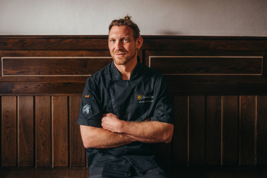 Wirt Michael Schindler, © Niederösterreich Werbung/Daniela Führer Ein Mann in schwarzer Kochjacke sitzt vor einer Holzwand.