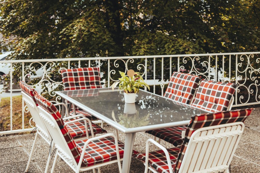 Auch ein Platz im Grünen steht bereit, © Niederösterreich Werbung/David Schreiber Gartentisch mit karierten Stühlen und Pflanze auf Terrasse.