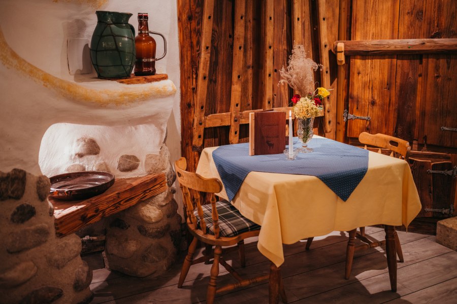 Seit 1977 ist der Bauernhof ein Gasthaus, © Niederösterreich Werbung/Daniela Führer Rustikales Gasthausinterieur mit Holzmöbeln, Tisch mit gelber Tischdecke, blauer Serviette, Blumen und Kerze.