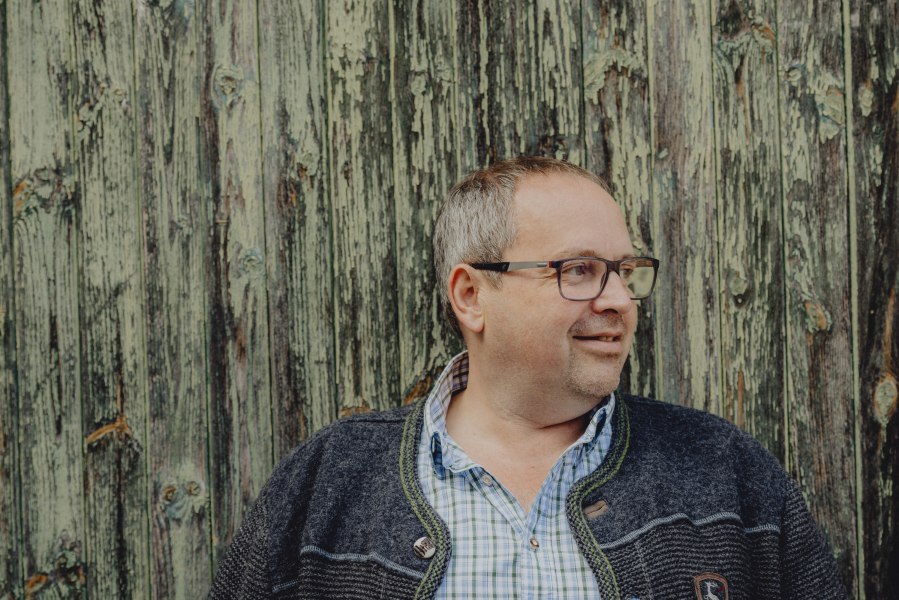 Wirt Erwin Hartl, © Niederösterreich Werbung/Rita Newman Mann mit Brille vor einer verwitterten Holzwand.