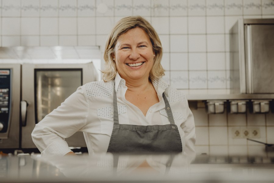 Wirtin Claudia Schilling, © Niederösterreich Werbung/Rita Newman Eine lächelnde Frau in einer Küche, die eine Schürze trägt.