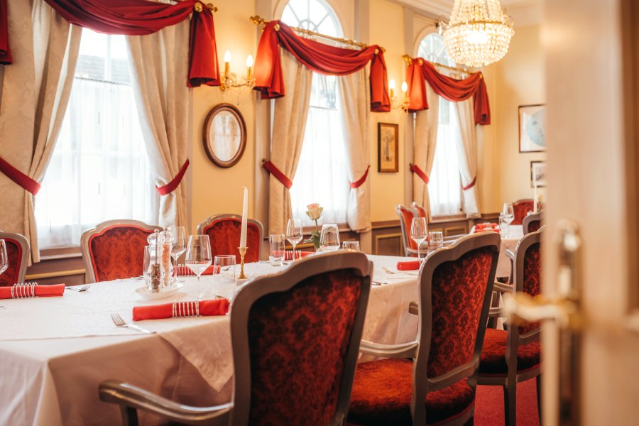 Feines Ambiente mit Feinschmecker-Menüs, © Niederösterreich Werbung/Daniela Führer Elegantes Restaurant mit gedecktem Tisch, roten Stühlen und Kronleuchter.