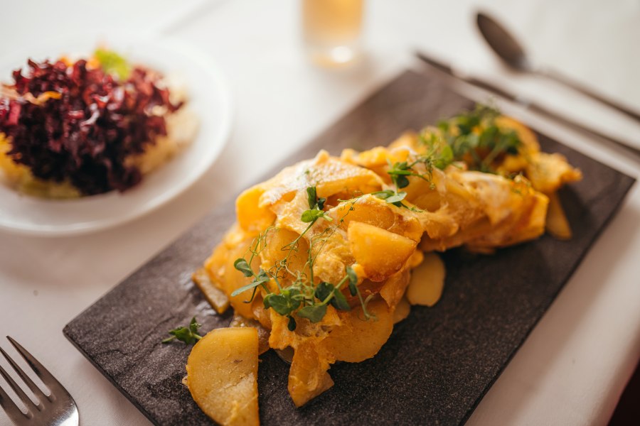 Geröstete Waldviertler Erdäpfelknödel, © Niederösterreich Werbung/Daniela Führer Geröstete Kartoffelscheiben mit Kräutern auf einem schwarzen Teller, daneben ein Salat.