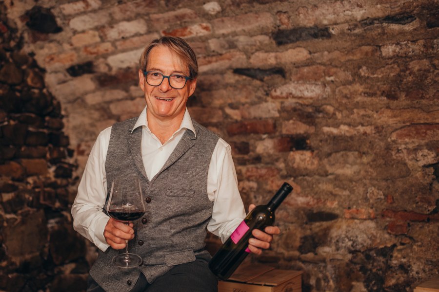 Wirt und Weinexperte: Martin Teufl, © Niederösterreich Werbung/Daniela Führer Ein Mann mit Brille hält ein Weinglas und eine Weinflasche vor einer Ziegelwand.