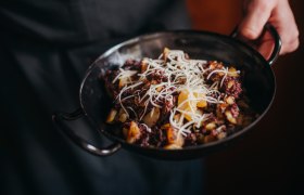 Blunzengröstl mit Sauerkraut, © Niederösterreich Werbung/Daniela Führer Eine Person hält eine Pfanne mit Blunzengröstl, garniert mit geriebenem Käse.