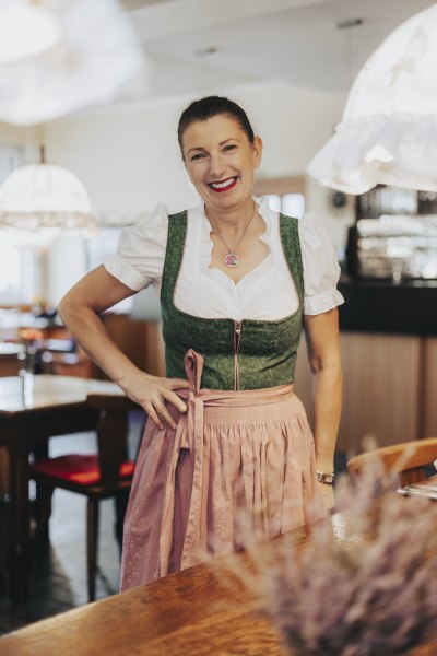 Wirtin Gabriele Großmann, © Niederösterreich Werbung/David Schreiber Eine lächelnde Frau in traditioneller bayerischer Tracht steht in einem Gastraum.