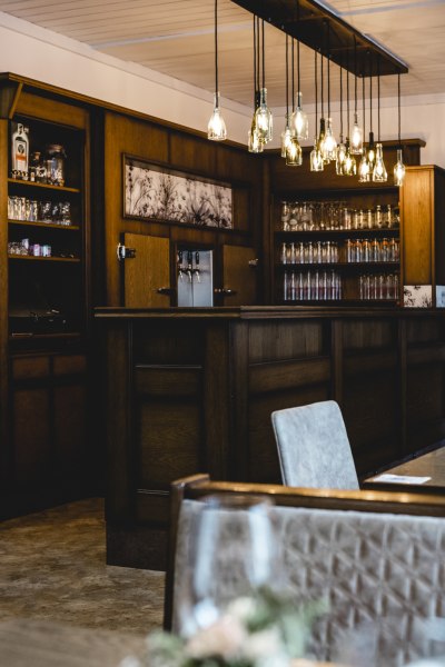 Besondere Wohlfühlatmosphäre, © Niederösterreich Werbung/David Schreiber Gemütliche Bar mit Holzmöbeln und hängenden Glühbirnen.