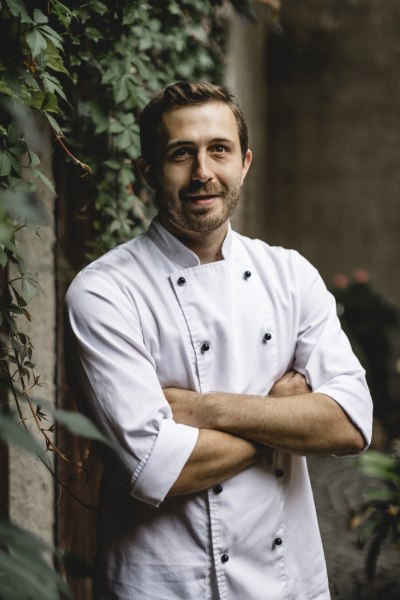 Stefan Fritsch achtet auf die hohe Qualität der Speisen, © Niederösterreich Werbung/David Schreiber Ein Koch in weißer Uniform steht mit verschränkten Armen vor einer mit Efeu bewachsenen Wand.