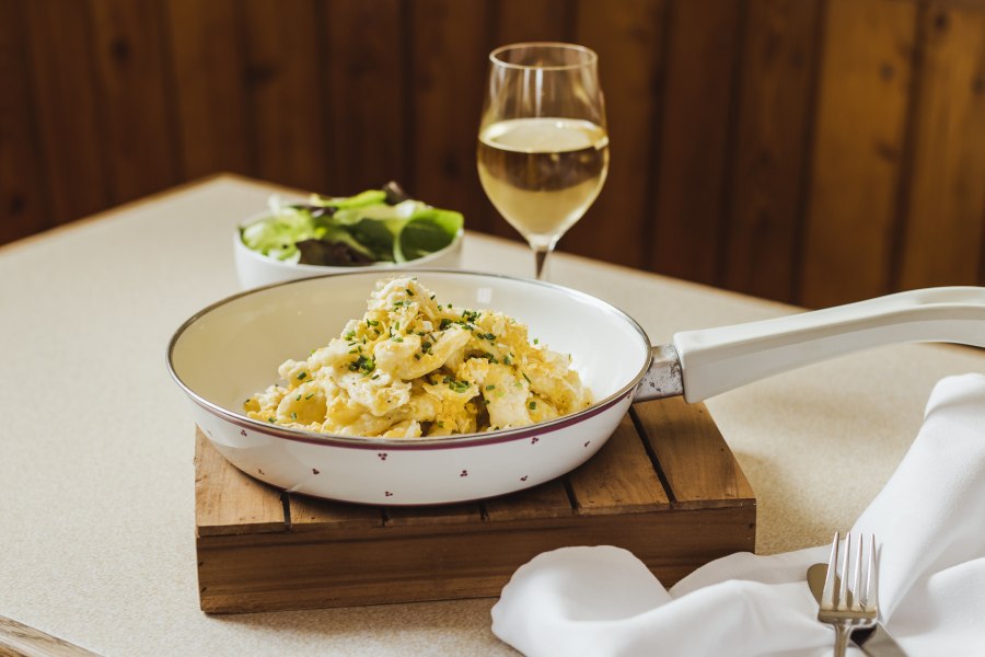 Beliebter Klassiker: Eiernockerl, © Niederösterreich Werbung/David Schreiber Eiernockerl in einer Pfanne mit einem Glas Weißwein und einem Salat im Hintergrund.