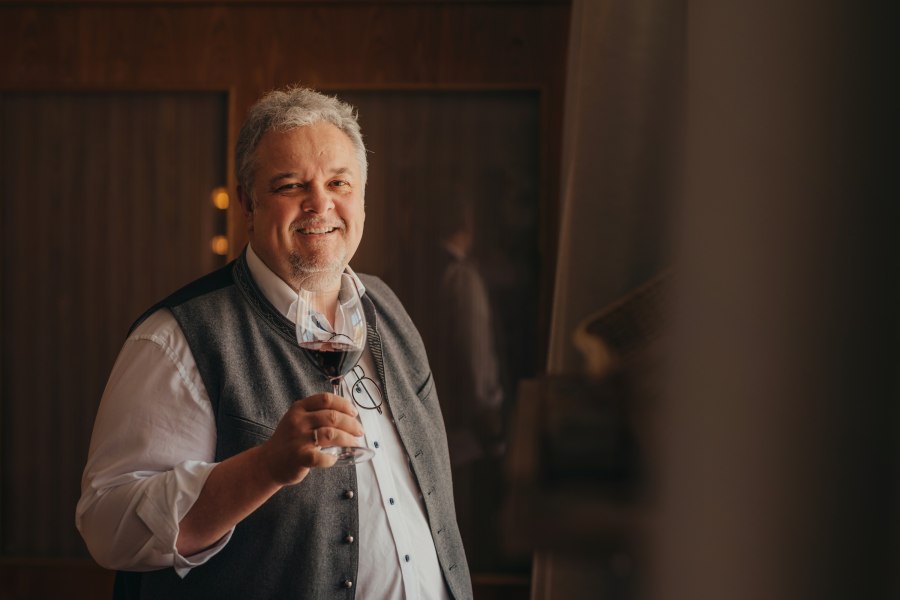 Wirt Karl Schwaighofer, © Niederösterreich Werbung/Daniela Führer Ein lächelnder Mann in traditioneller Kleidung hält ein Glas Rotwein.