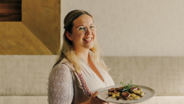 Wirtin Sabrina Stadler, © Niederösterreich Werbung/Julius Hirtzberger Frau in traditioneller Kleidung serviert ein Gericht auf einem Teller.