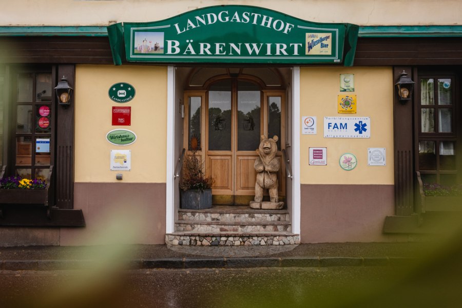 Haubenlokal in Petzenkirchen, © Niederösterreich Werbung/Daniela Führer Eingang des Landgasthofs Bärenwirt mit Holzfigur eines Bären und verschiedenen Schildern an der Wand.