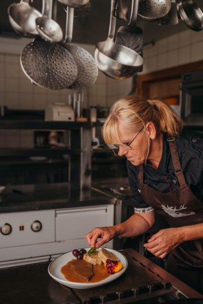Wirtin Ulrike Distelberger, © Niederösterreich Werbung/Daniela Führer Eine Frau in einer Küche richtet ein Gericht auf einem Teller an.