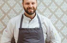 Chefkoch und Wirt Philipp Essl, © Niederösterreich Werbung/Michael Reidinger Philipp Essl in Kochkleidung steht vor einer gemusterten Tapete.